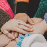 dłonie kilku osób ułożone jedna na drugiej w geście wpsólnoty;